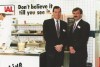 A trade show photo from 1994 in the USA featuring two men in suits standing in front of a kitchen setup, with a chef preparing food in the background.