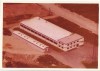 An aerial view of a factory building from 1973, showing a large main building with a flat roof and an adjacent smaller structure, surrounded by dirt paths and greenery.