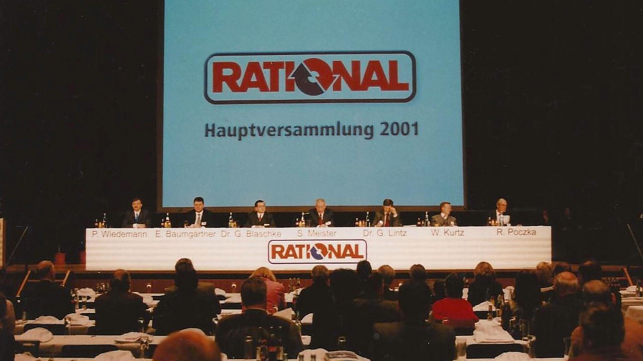 A scene from the 2001 Rational annual meeting featuring a panel of speakers at a long table, with attendees in the audience.