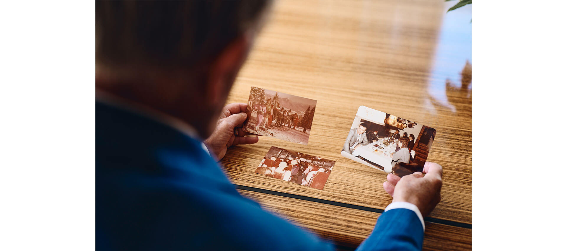 Person in a blue suit holding vintage photographs while sitting at a wooden table, reminiscing about past events.
