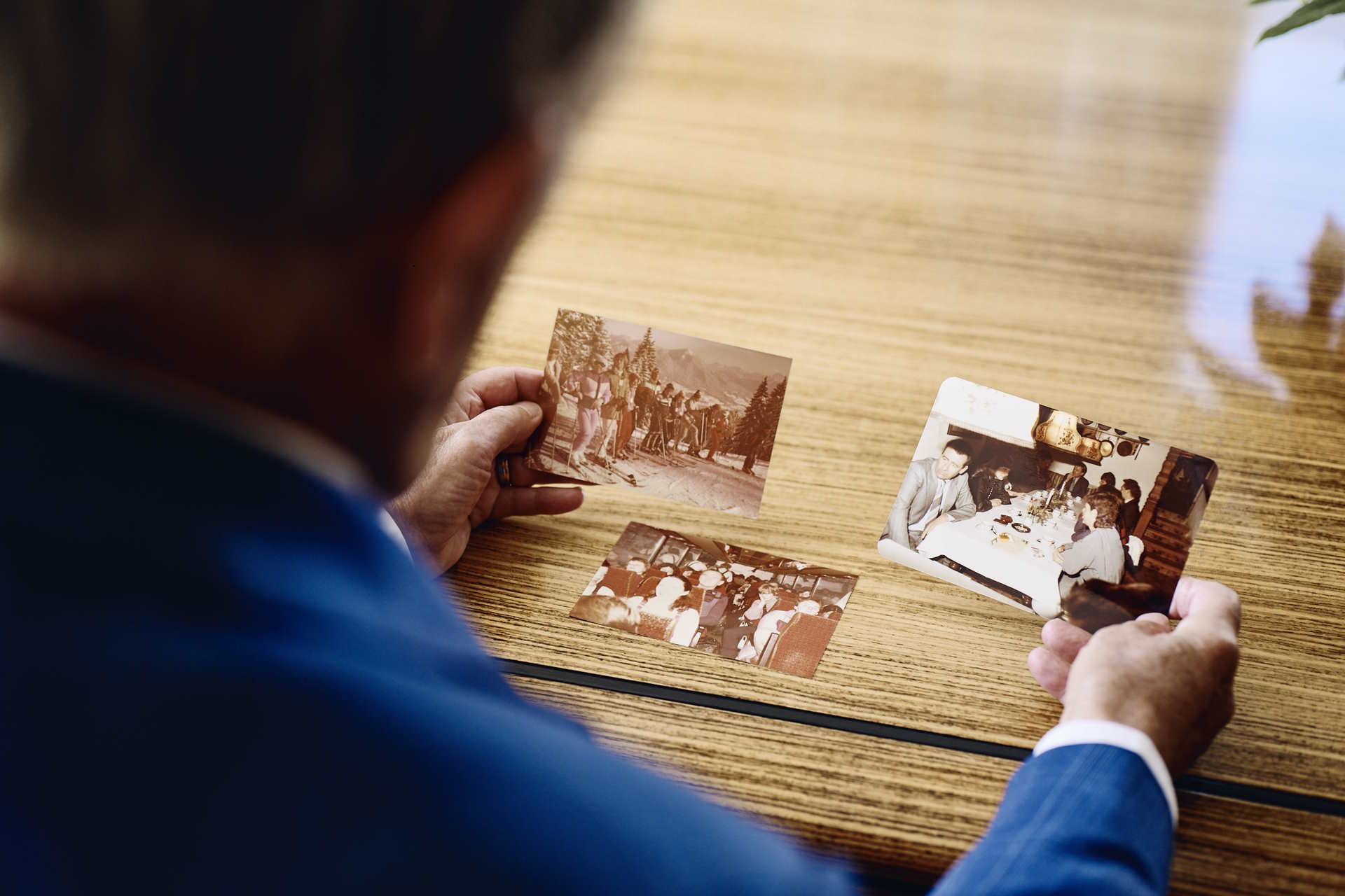 Person in a blue suit holding vintage photographs while sitting at a wooden table, reminiscing about past events.