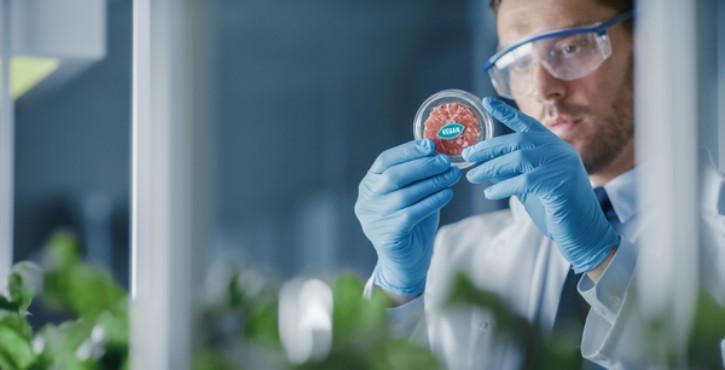 A scientist in a laboratory examines a petri dish containing a lab-grown cultured vegan meat sample.