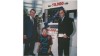 Three people celebrating the sale of the 50,000th Rational combi-steamer in 1991, with a large banner in the background.