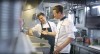 Two chefs in a commercial kitchen, one in a white chef‘s coat and the other in a black apron, discussing food preparation over a iVario Pro.