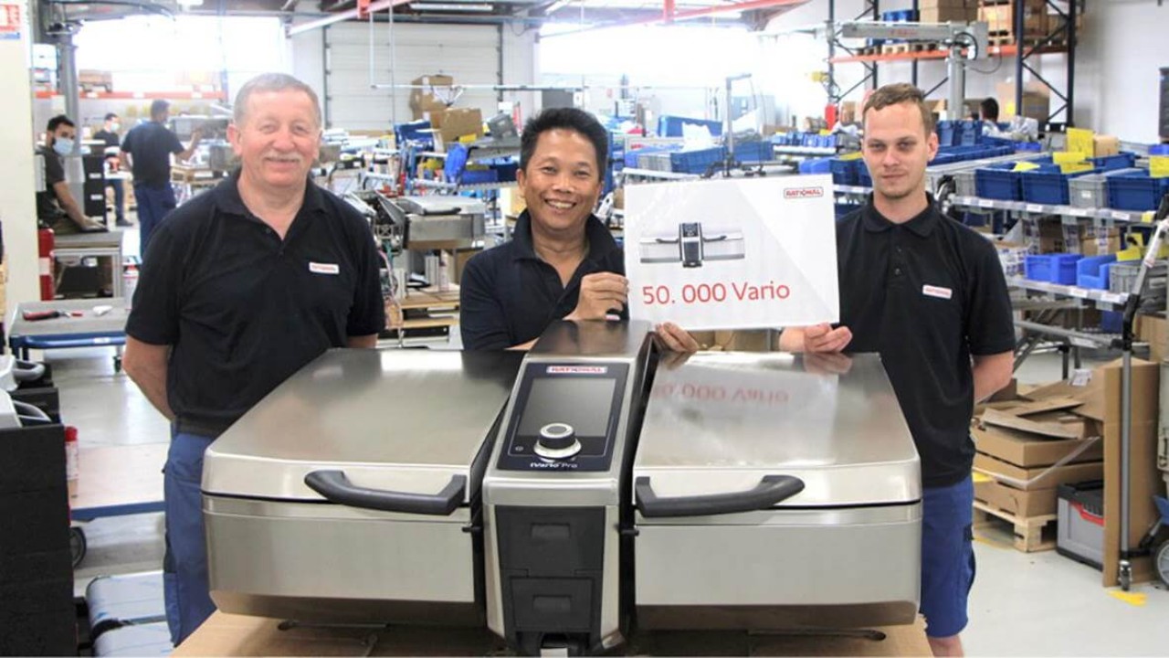 Three men in a factory setting pose with a Vario cooking appliance, celebrating the production of the 50,000th unit.