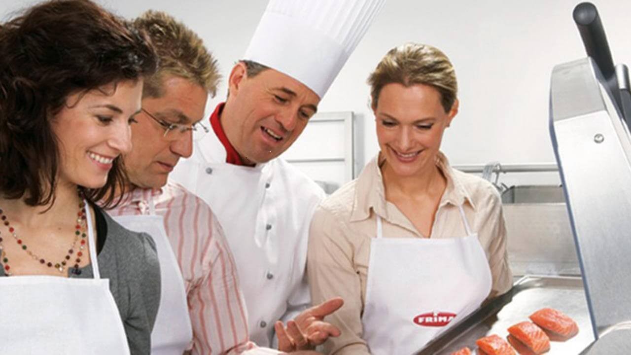 Group of four people, including a chef, examining prepared salmon fillets in a kitchen setting, wearing aprons.