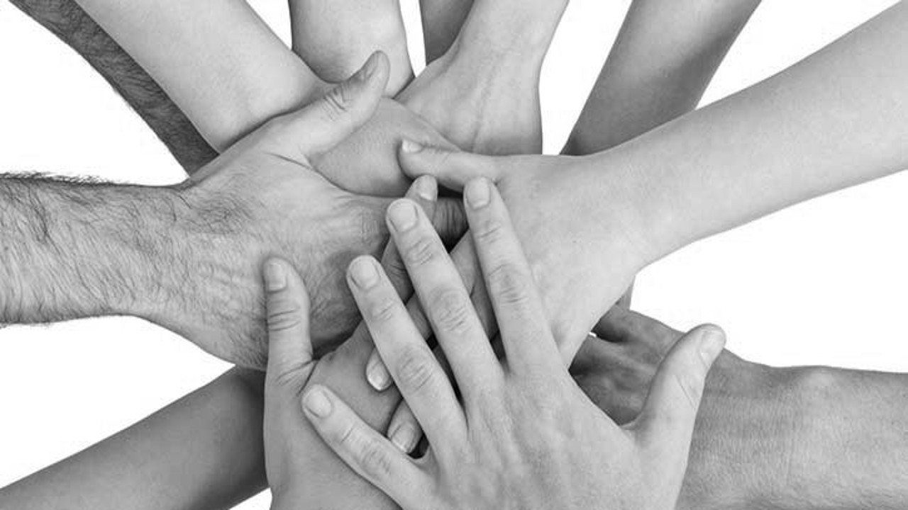 A black and white image showing multiple hands of different sizes and skin tones coming together in a collaborative gesture.