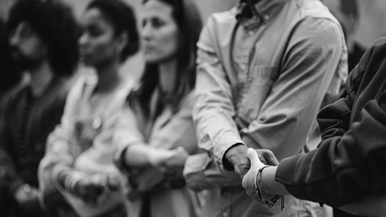 A black and white image of a diverse group of people holding hands, symbolizing unity and solidarity in support of human rights.