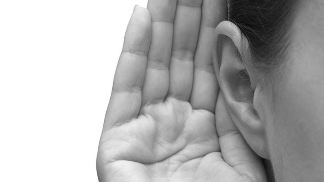 A black and white close-up of a hand cupped behind an ear, symbolizing the act of listening attentively.