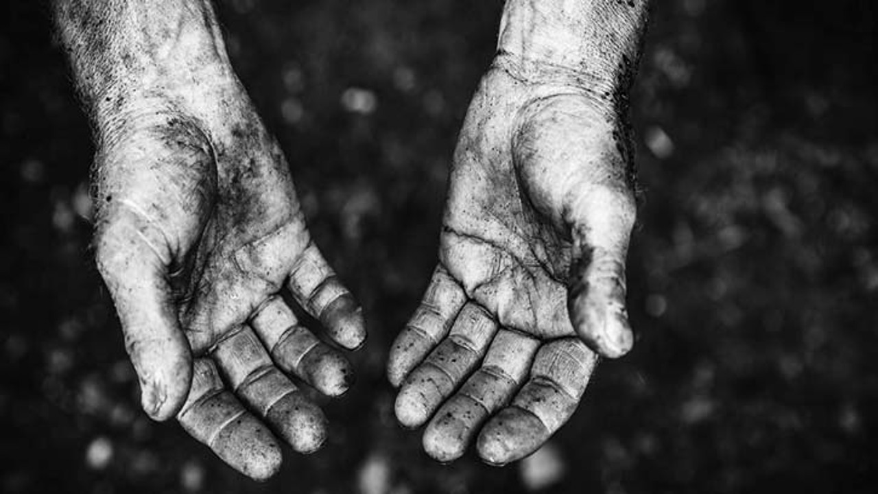 A black and white close-up of dirty hands held open, symbolizing vulnerability and the plight of laborers in difficult conditions.