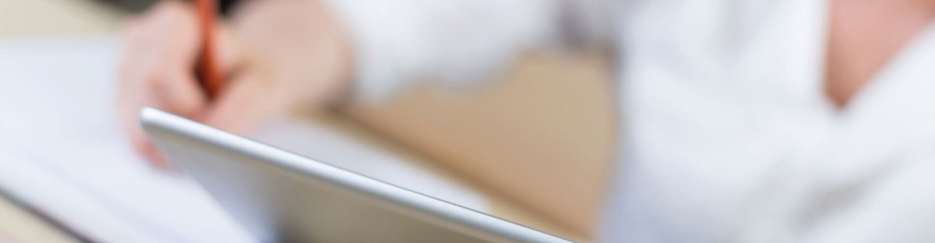 Person hält Tablet und schreibt mit Bleistift Notizen in einen Block, Lern- oder Arbeitssituation.