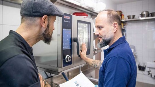 Dos hombres conversando frente a un iCombi Pro en una cocina profesional.