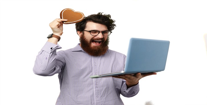 Hombre feliz con gafas y laptop, levantando un corazón de pan de jengibre.