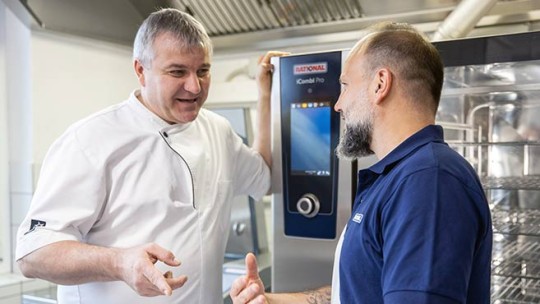 Two men talking in front of a Rational iCombi Pro oven.