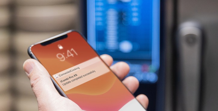 Hand holding a smartphone with a notification about a successful ConnectedCooking update.