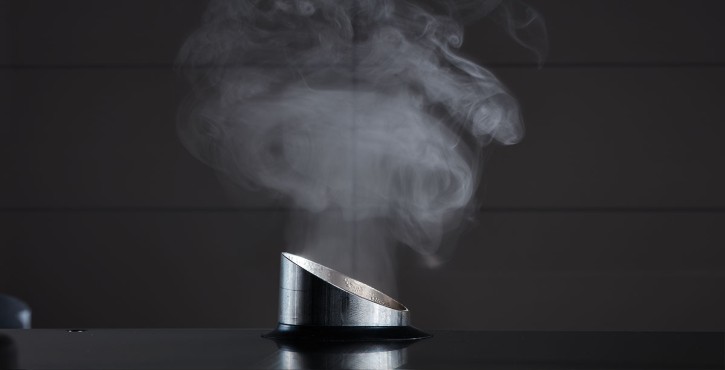 A stainless steel steam outlet releasing steam into the air against a dark background.