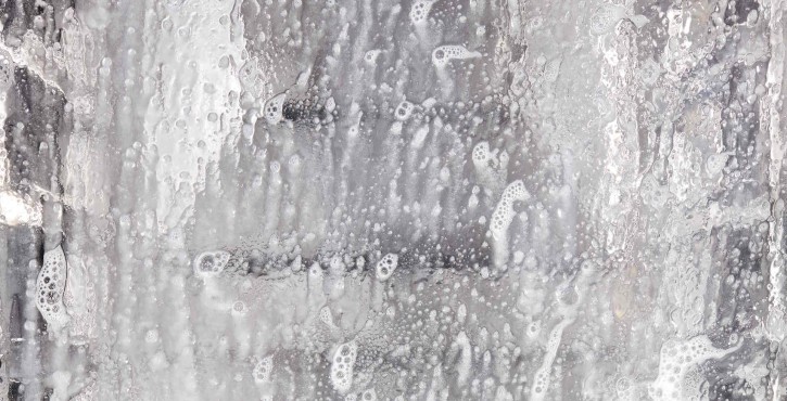  Close-up of a glass surface with water droplets and soap bubbles, reflecting light and creating a textured appearance.