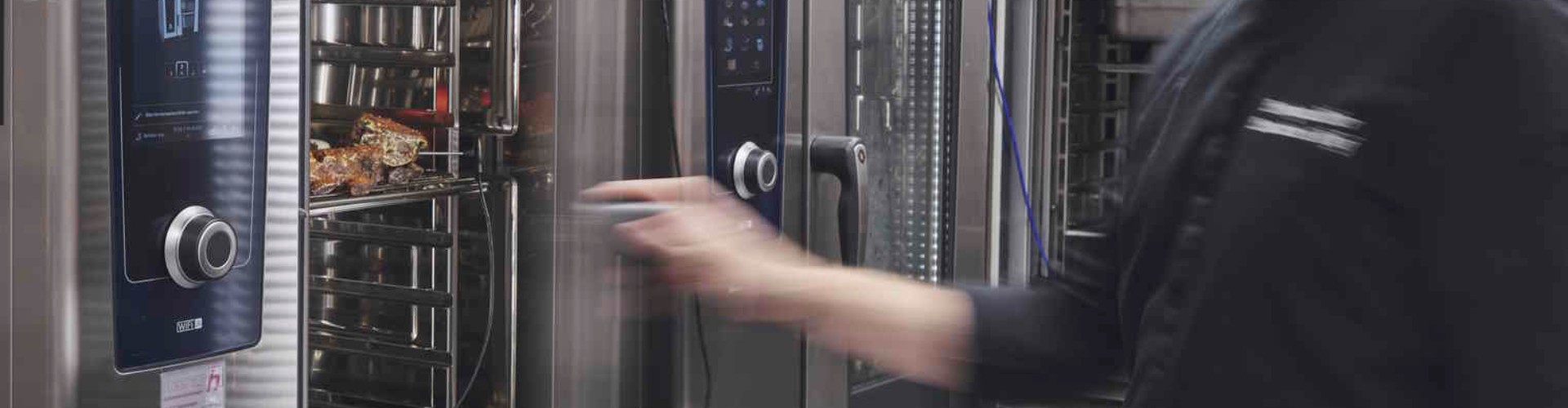 A chef in a black uniform operates an iCombi Pro oven in a kitchen, loading trays while checking the display.