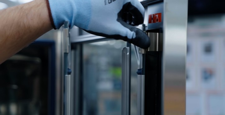 A close-up of a hand wearing a glove adjusting the door latch of a Rational cooking oven.