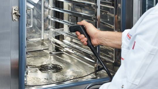 Using a hand shower to clean the interior of an iCombi Pro oven.