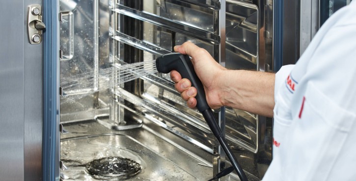 Using a hand shower to clean the interior of an iCombi Pro oven.