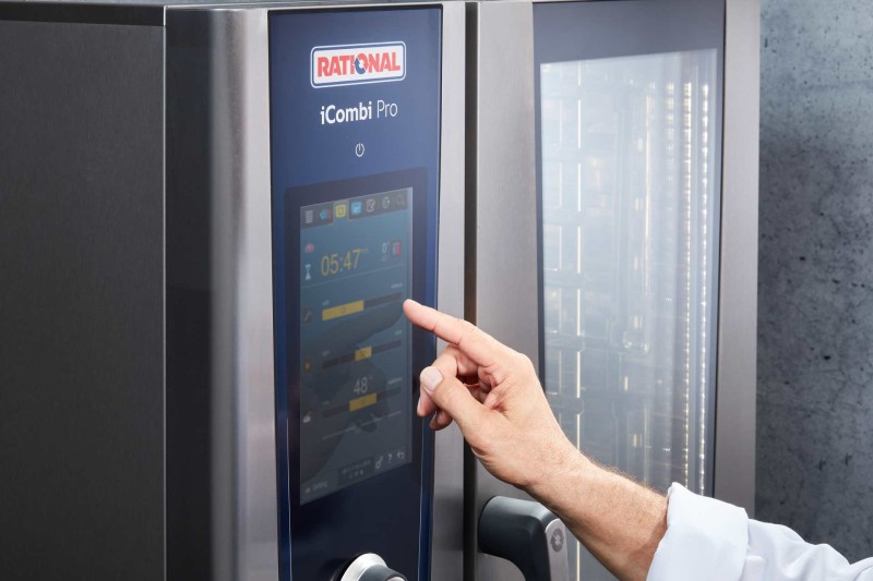 Main utilisant l’écran tactile du RATIONAL iCombi Pro four mixte avec affichage des paramètres de cuisson.