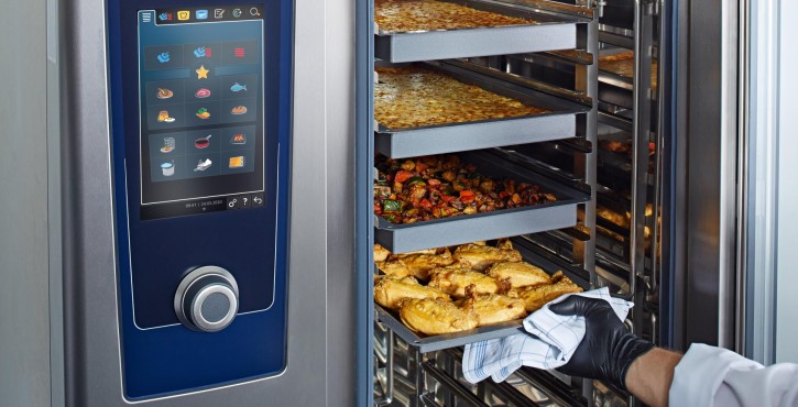A chef using a Rational iCombi Pro, pulling out trays of food including chicken, roasted vegetables, and baked items from the cooking unit.