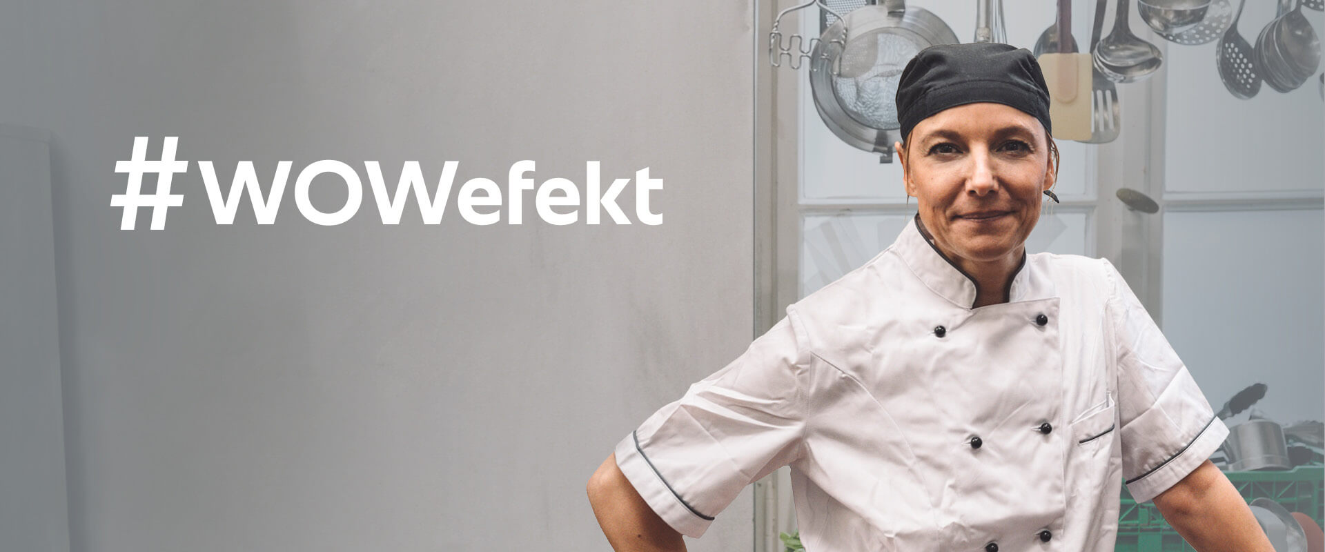 A female chef wearing a white uniform and a black chef hat stands confidently with her arms crossed, beside the text '#TheWOWeffect' in a kitchen filled with cooking utensils.