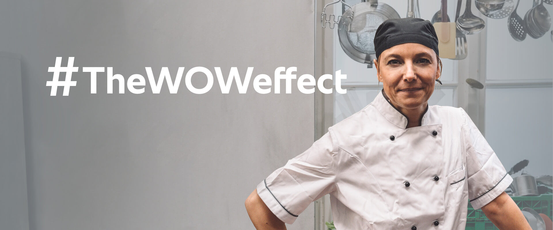 A female chef wearing a white uniform and a black chef hat stands confidently with her arms crossed, beside the text '#TheWOWeffect' in a kitchen filled with cooking utensils.