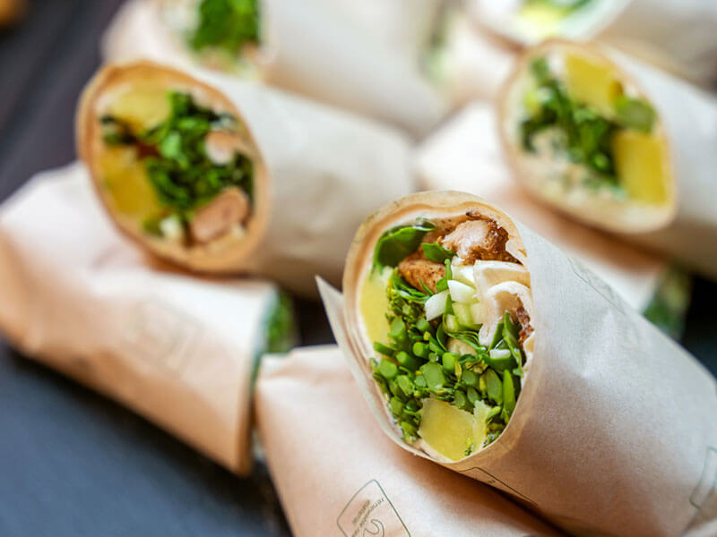 Wraps frescos de verduras y pollo en papel, rellenos de vegetales y papas en cubos.
