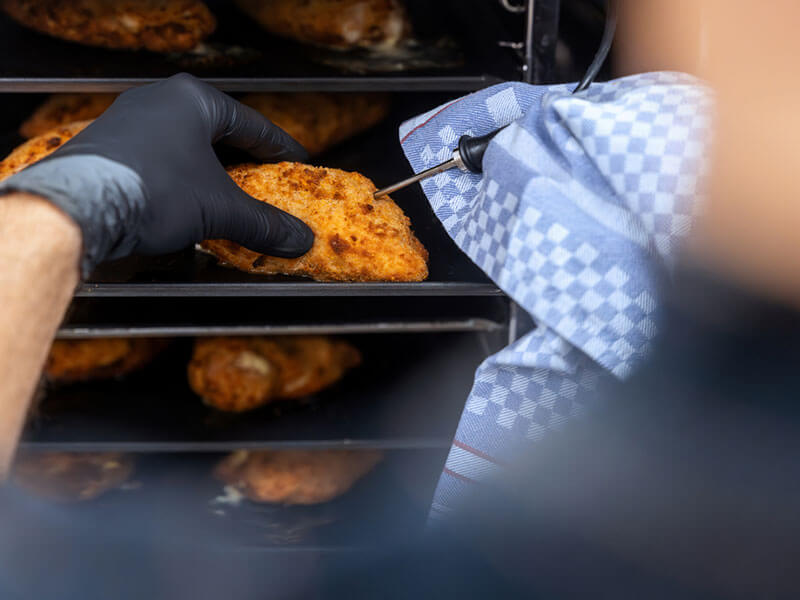 Koch überprüft mit einem Temperaturfühler das knusprige panierte Hähnchen in einem RATIONAL Kombidämpfer.