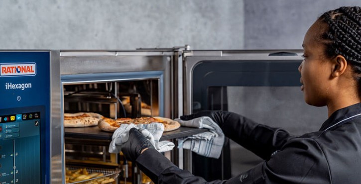Chef in a black uniform removing freshly baked pizzas from a RATIONAL iHexagon combi-steamer.