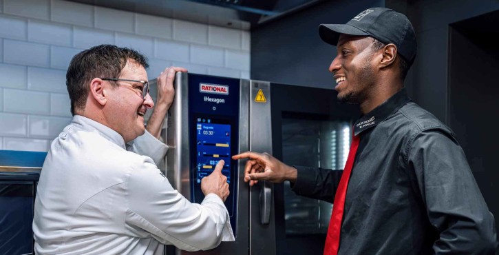 Two chefs using the touchscreen of a RATIONAL iHexagon combi oven in a professional kitchen.