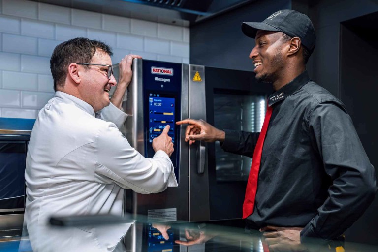 Deux chefs utilisent l’écran tactile d’un RATIONAL iHexagon four mixte dans une cuisine professionnelle.