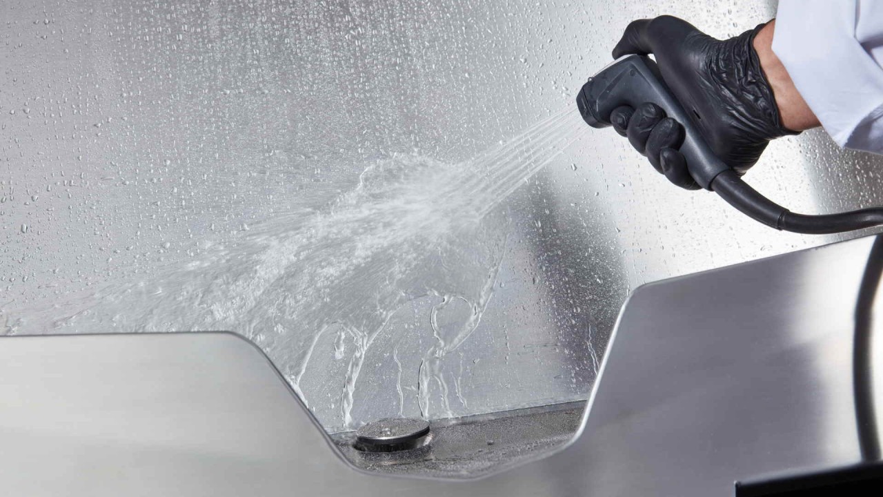 A close-up of a hand using a hand shower to clean the interior of the Rational iVario Pro cooking appliance.
