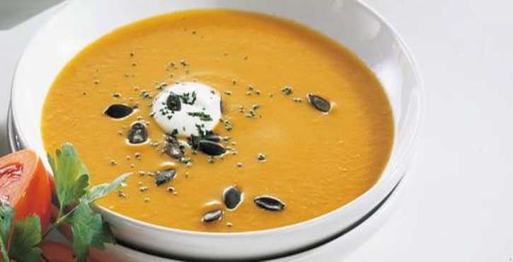 Un bol de soupe de potiron crémeuse, garnie d'herbes et d'épices autour des bords.