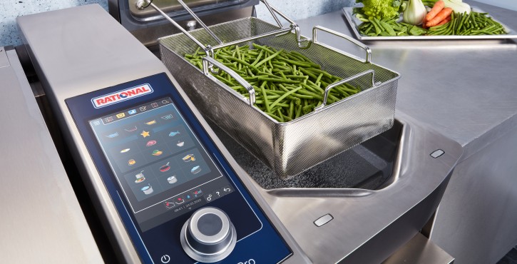 A close-up view of the Rational iVario Pro appliance with a basket of green beans being cooked, featuring a modern control panel.