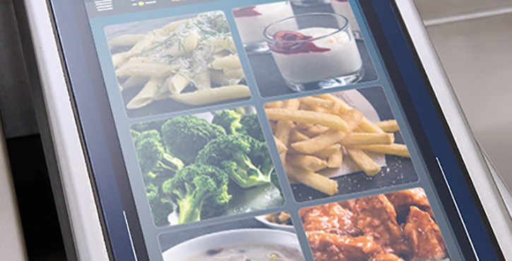 A close-up of the Rational iVario Pro cooking appliance's display panel showing various food images, including pasta, broccoli, fries, and dessert.