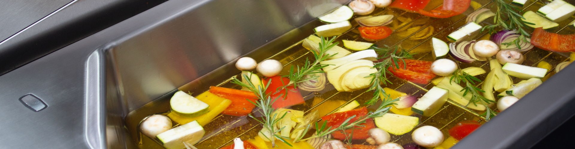 Ein Tiegel voller bunter Gemüse, darunter Zucchini, Paprika, Zwiebeln und Champignons, in Öl eingelegt und mit Rosmarin garniert.
