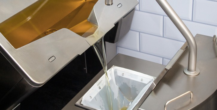 A close-up of the oil drainage system from a Rational iVario Pro appliance, showing oil being drained into a container.