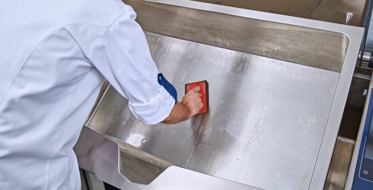 Un chef limpiando la superficie de acero inoxidable de un aparato Rational iVario Pro con una esponja, demostrando el mantenimiento adecuado de la cocina.