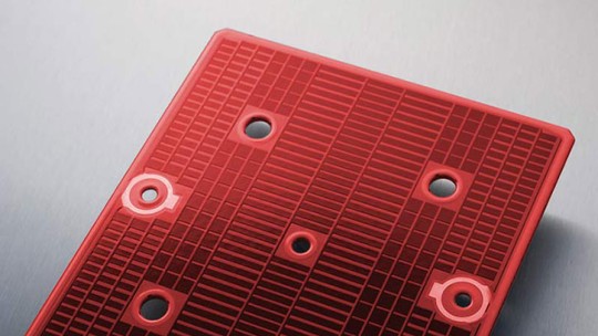A close-up of a red heating unit with circular holes and a textured surface for cooking.