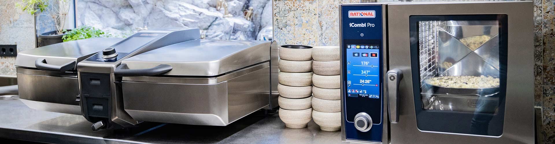 A Rational iCombi Pro cooking system next to a iVario Pro, with stacked ceramic bowls in a modern kitchen setting.