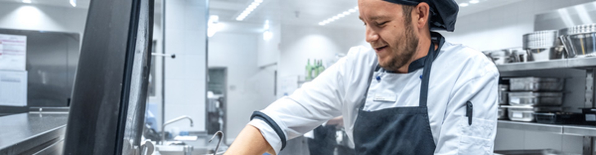 Chef lifting fryer baskets at a steam-filled cooking station in a commercial kitchen.