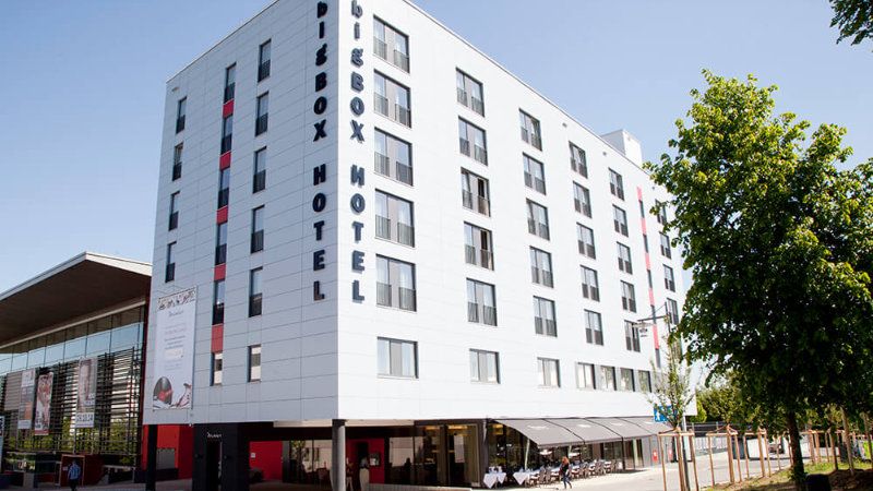 Außenansicht des BigBox Hotels mit Bäumen und klarem blauen Himmel.