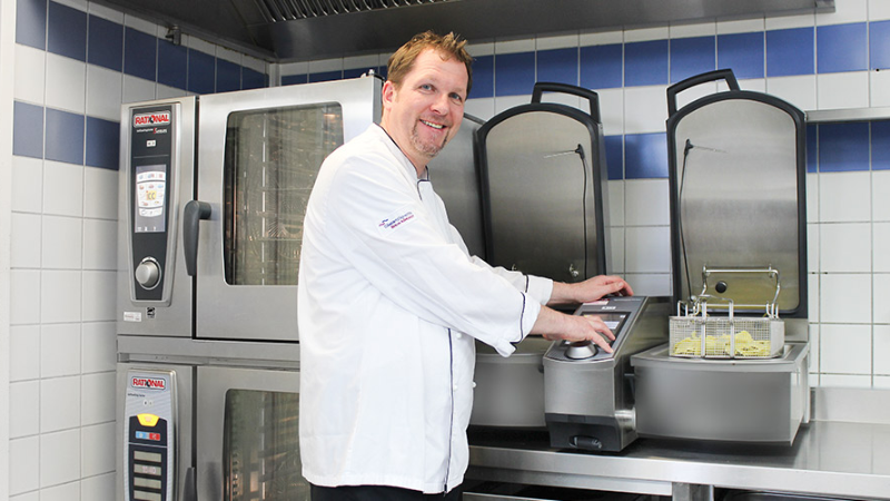 Chef smiling while using a Rational cooking appliance in a professional kitchen.