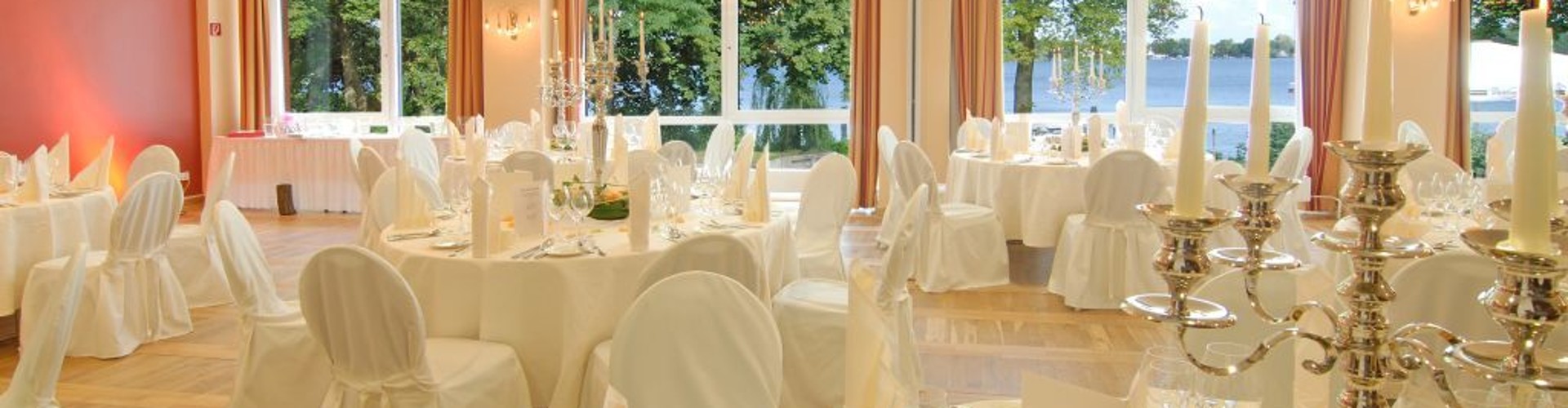 Elegant banquet hall with round tables, white linens, and a lake view.