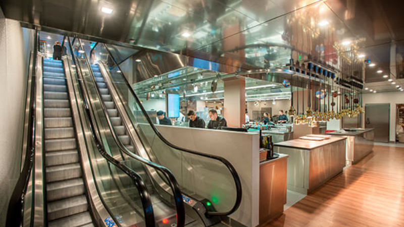 Modern kitchen area next to escalators in a stylish restaurant interior.