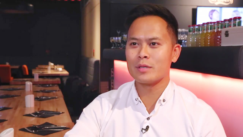 A man in a white shirt sitting in a restaurant with a blurred background.