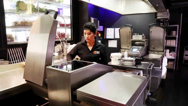 A woman in a black shirt working in a kitchen with stainless steel equipment.
